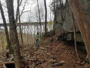 A hiker on rocky trail about to pass under a large bridge