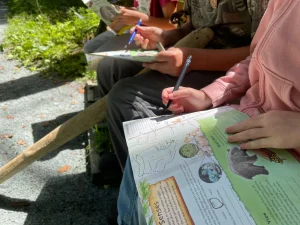 Several children write in their Limberlost TRACK Trails booklets while resting on a bench.